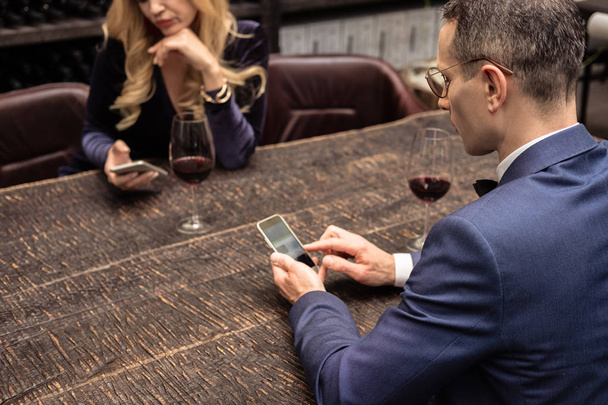 unhappy adult couple using smartphones on date at restaurant - Photo, Image