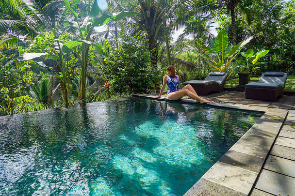 A young girl sits on the edge of an infinity pool in the jungle. Taken on the island of Bali in Ubud. - Foto, Bild