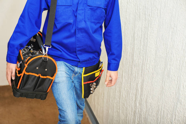 Young plumber with tool bag and belt, indoors - Fotoğraf, Görsel