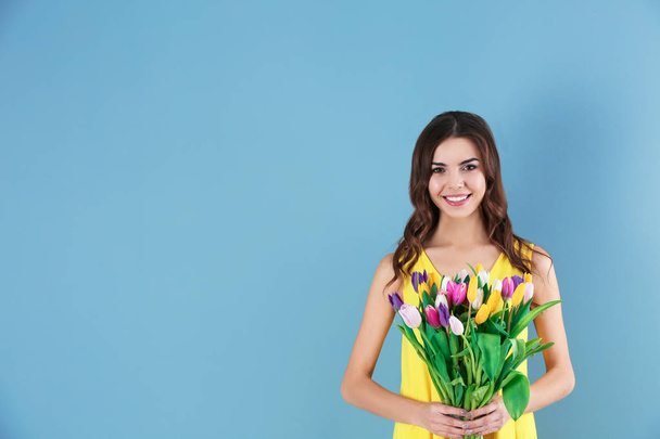 Beautiful woman holding bouquet of tulips on color background - Фото, зображення