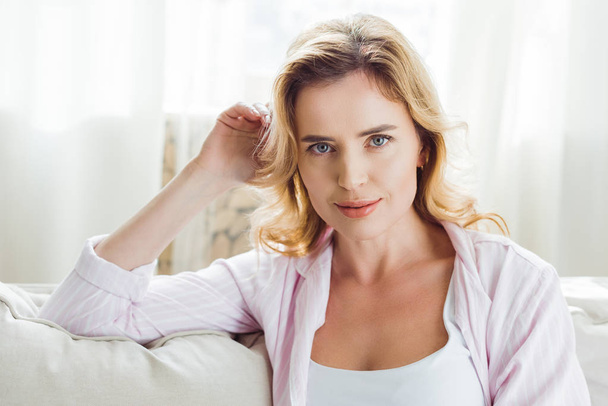 blonde woman in pajamas sitting on sofa at home - Zdjęcie, obraz