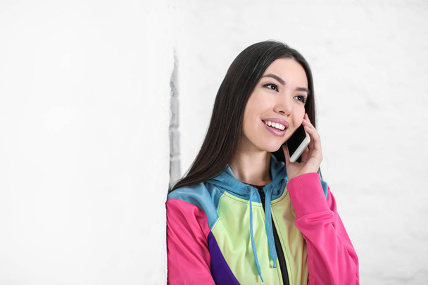 Beautiful young woman talking on mobile phone near white wall - Fotoğraf, Görsel