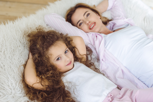 ευτυχισμένη κόρη και όμορφη μητέρα ξαπλωμένος σε κουβέρτα δερμάτων προβάτων - Φωτογραφία, εικόνα