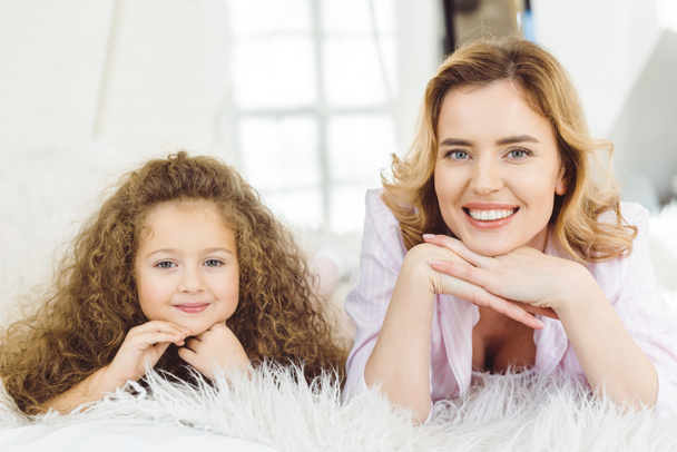 smiling mom and adorable curly daughter lying and looking at camera - Fotografie, Obrázek