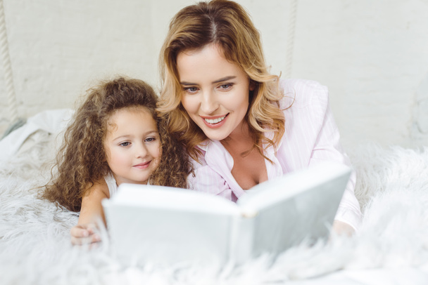 mother and curly daughter reading book together - Фото, изображение