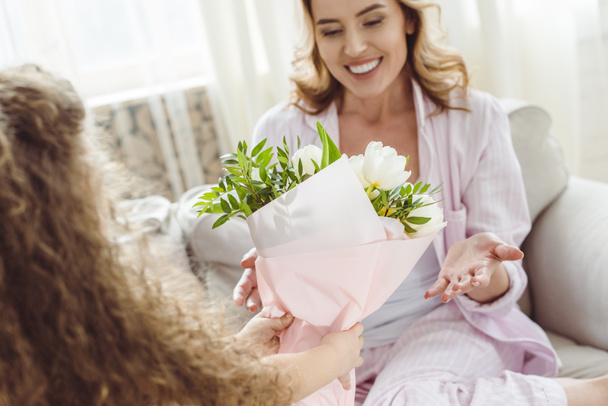 fille présentant bouquet de fleurs à sa maman souriante le jour de la fête des mères heureuses
 - Photo, image