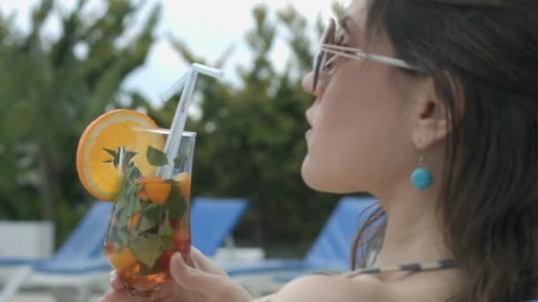 Girl enjoying taste of cool cocktail sitting by pool of her luxurious mansion - 映像、動画