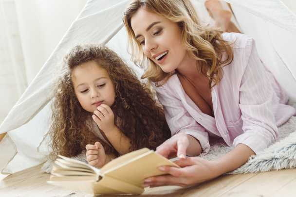 beautiful mother and daughter reading book in kid wigwam - Zdjęcie, obraz