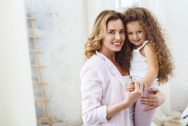 beautiful happy mother holding on arms her smiling curly daughter  - Фото, зображення