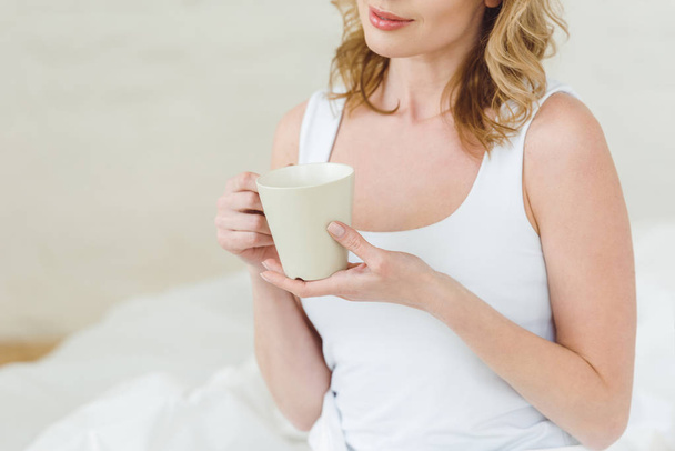 cropped view of woman with cup of coffee in bedroom in the morning - Foto, immagini