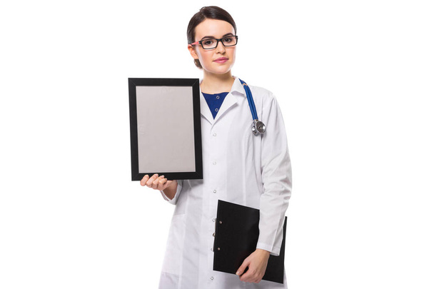 Young confident female doctor holding blank frame and clipboard  - Фото, зображення
