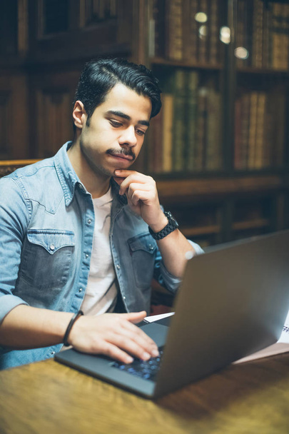 Розумний молодий арабський чоловік працює в бібліотеці з комп'ютером
 - Фото, зображення