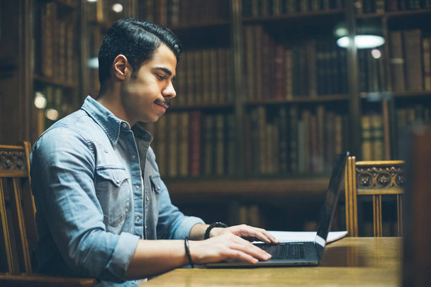 Education in Europe. arabic young handsome working in old library. Horizontal composition. View from side profile - Foto, imagen