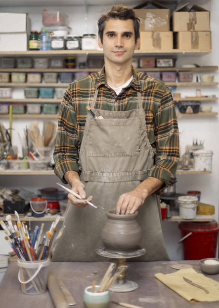 Jonge man maken en decoreren van aardewerk in werkplaats - Foto, afbeelding