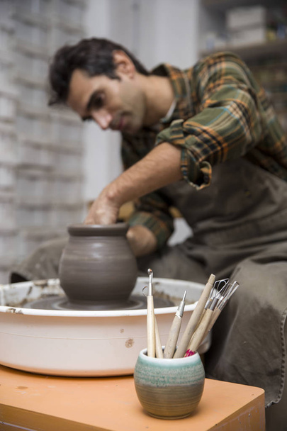 View at an artist makes clay pottery on a spin wheel in workshop - Foto, immagini
