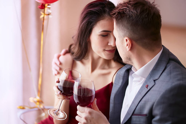 Beautiful couple celebrating Valentine`s day in restaurant, drinking wine, sharing gifts and enjoying each other. - Foto, Imagem