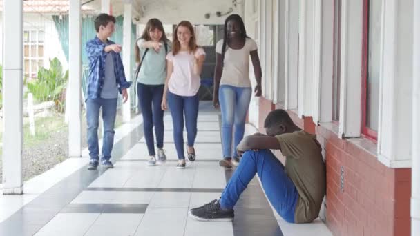 group of teenagers walking in school hallway and bullying a boy sitting on the floor  - Video