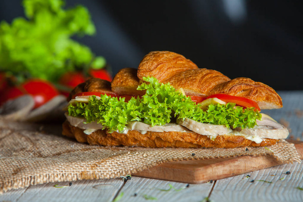 Croissant sendviče podávané na dřevěném prkénku. Croissanty s vejce, strouhaným sýrem, petrželkou, kuřecí šunka, uzený losos - Fotografie, Obrázek