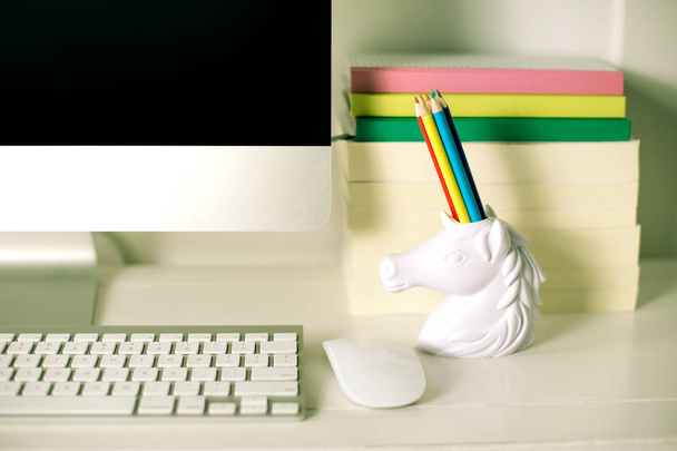 workspace front view computer keyboard mouse and unicorn pencil holder and books on background, rainbow colours - Photo, image