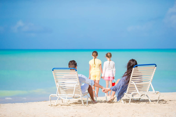 Família bonita feliz de quatro na praia. Pais relaxantes na cama de sol e crianças se divertindo na costa
 - Foto, Imagem