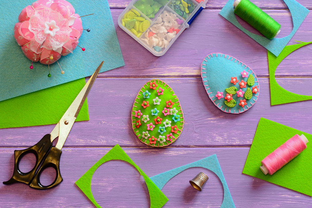 Creative Easter egg ornaments with plastic flowers and leaves. Felt eggs with floral pattern, scissors, thread on the wooden table. How to decorate home for Easter. Sewing concept workplace. Tailor workplace. Hand sewing concept workplace - Photo, Image