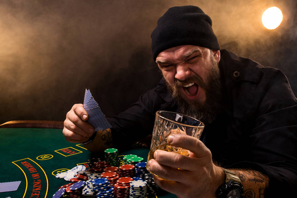 Szakállas férfi szivar és üveg egy kaszinó póker asztalnál. Szerencsejáték, kártya és a rulett. - Fotó, kép