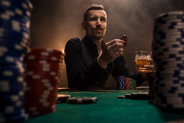 Όμορφος νεαρός που κάθονται πίσω από το τραπέζι πόκερ με κάρτες και μάρκες - Φωτογραφία, εικόνα