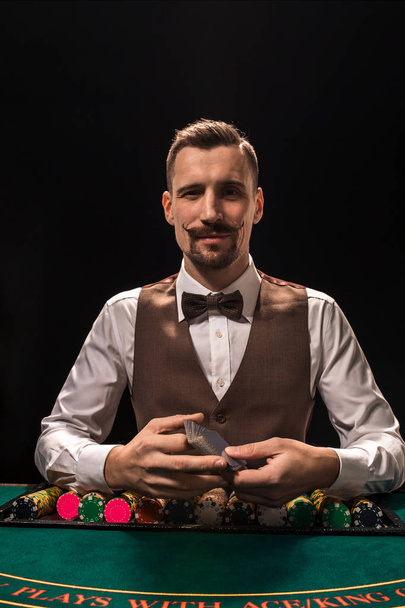 Retrato de un croupier es la celebración de cartas, fichas de juego en la mesa. Fondo negro
 - Foto, imagen