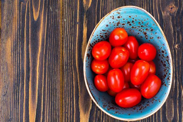 Mały czerwony dojrzałe pomidory w misce na drewnianym stole, widok z góry - Zdjęcie, obraz