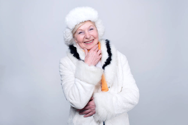 Happy old woman with a smile on her face. Smiling woman in warm winter clothes standing on a light background. - Photo, Image