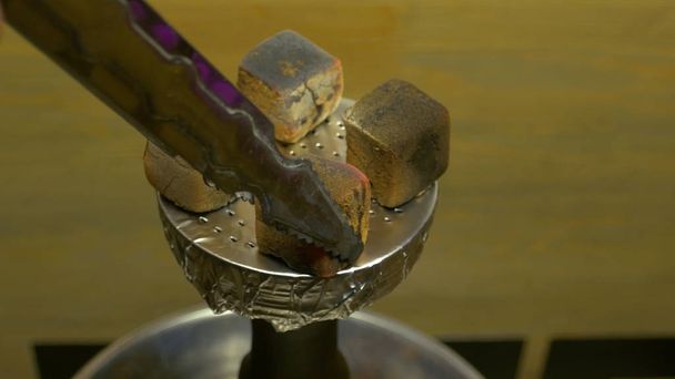 Mans hand puts burning coals on clay bowl with tobacco for hookah, Hookahs head. Hookah topic: Bartender holding a forceps with coal for hookah and puts them into a clay bowl - Photo, Image
