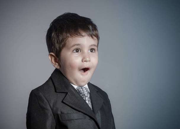 first employment, little businessman, brown-haired boy dressed in suit and tie with faces and funny expression - Foto, afbeelding