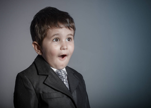 eerste werkgelegenheid, kleine zakenman, bruinharige jongen gekleed in pak en stropdas met gezichten en grappige expressie - Foto, afbeelding