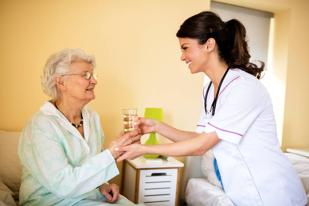 Enfermeira traz água para paciente idoso
 - Foto, Imagem