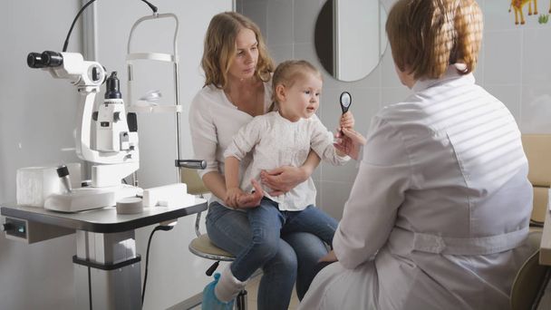 Menina e sua mamãe em oftalmologia optometrista verificando pequena visão infantil
 - Foto, Imagem