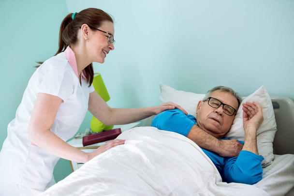 Nice smiling nurse looking at patient who sleeping and dreaming - Fotó, kép