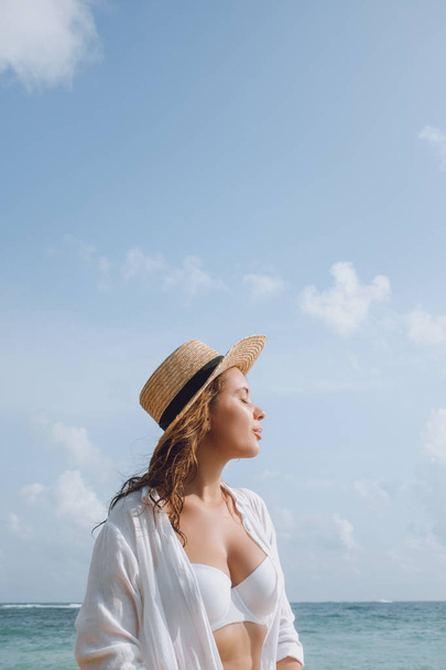 Young woman in a white bathing suit and hat sunbathing on the beach - Foto, Imagen