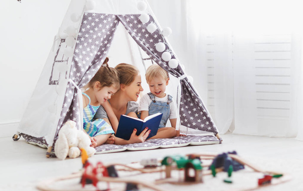 familia madre leyendo a los niños libro en tienda de campaña en casa - Foto, Imagen