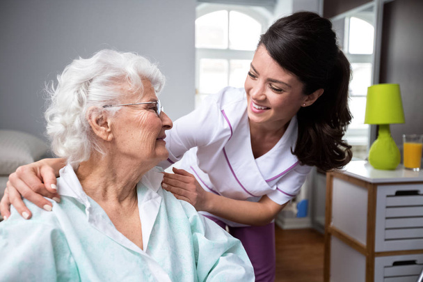 Smiling nurse and old woman patient at wheelchair - Foto, Bild