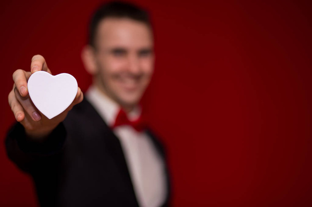 Stylish man in suit holding love gift box with red background, focus on gift box. Valentines day composition. Offer of marriage - Fotografie, Obrázek