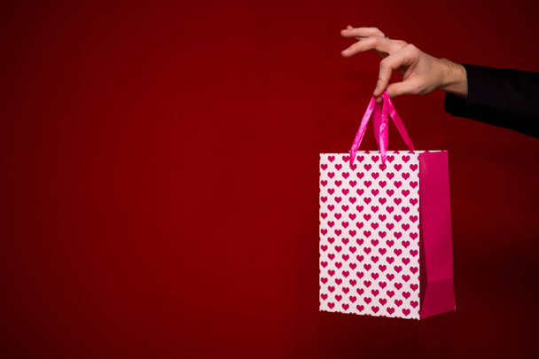 La mano del hombre sostiene la bolsa de regalo de amor, con fondo rojo, se centran en la bolsa de regalo. San Valentín composición del día
 - Foto, imagen