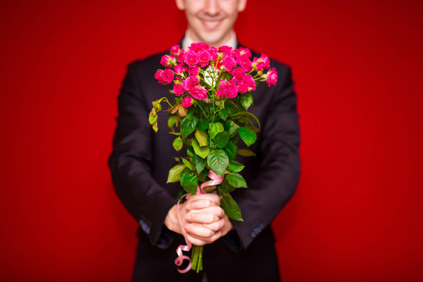 Стильний чоловік у костюмі, що тримає букет квітів з червоним тлом, фокус на квітах
 - Фото, зображення