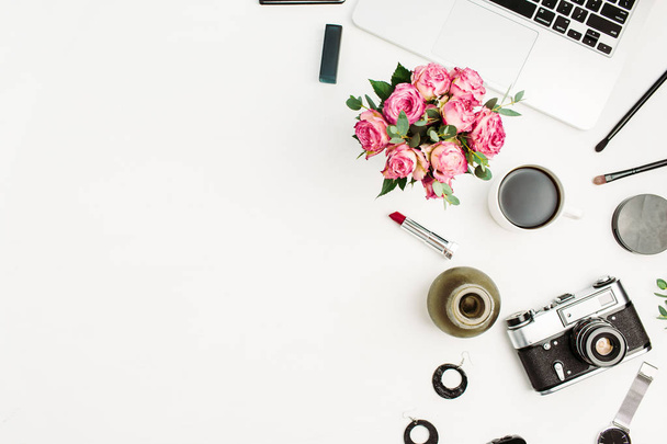 Vrouw mode kantoor aan huis Bureau. Werkruimte met laptop, roze bloemen boeket, retro camera, accessoires en cosmetica op witte achtergrond. Plat lag, top uitzicht stijlvolle vrouwelijke mockup. - Foto, afbeelding