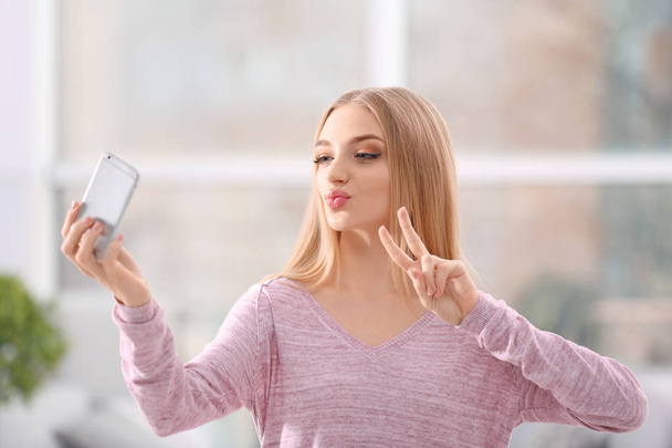 Young woman taking selfie on cell phone indoors - Foto, imagen
