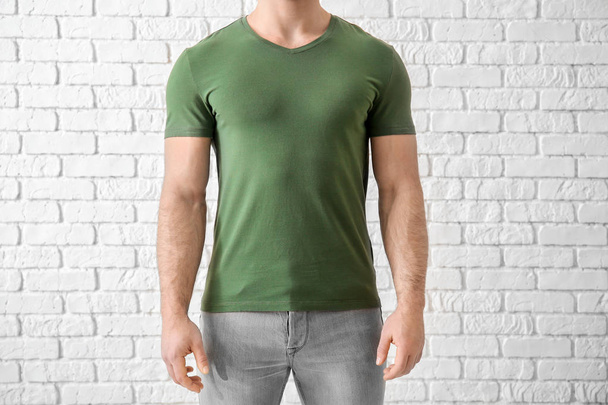 Young man in stylish t-shirt near white brick wall. Mockup for design - Photo, Image