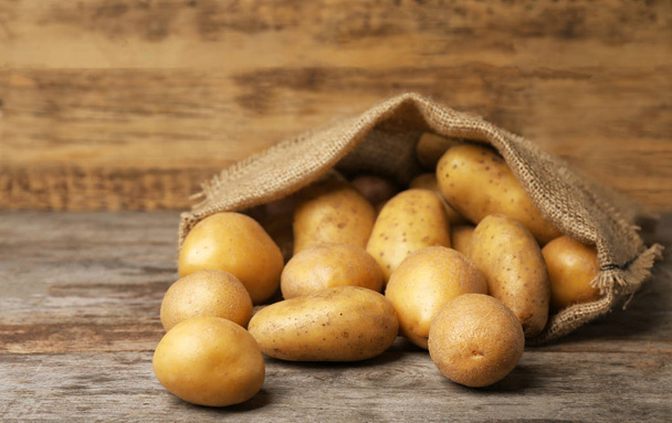 Sack of fresh raw potatoes on wooden table - Фото, изображение