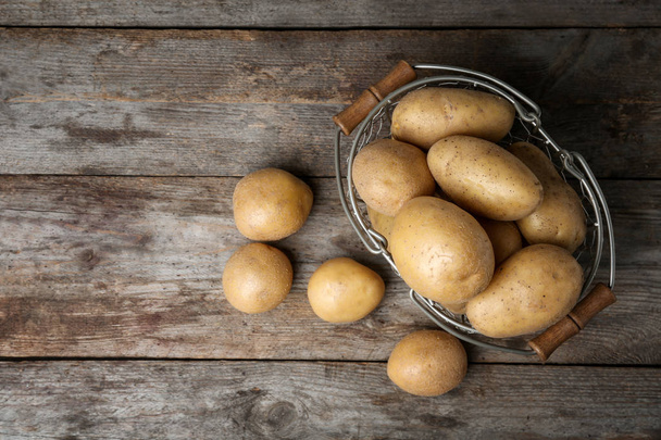 Mand met verse rauwe aardappelen op houten achtergrond, bovenaanzicht - Foto, afbeelding
