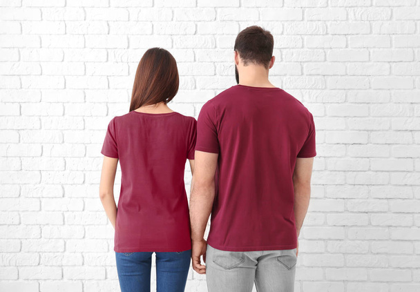 Young man and woman in stylish t-shirts near white brick wall. Mockup for design - Foto, immagini