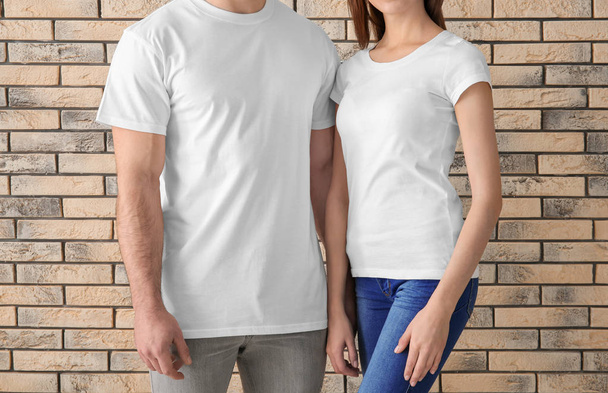 Young man and woman in stylish white t-shirts near brick wall. Mockup for design - Foto, Imagen