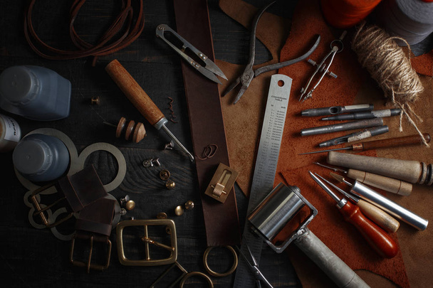 Ensemble d'outils artisanaux en cuir sur fond en bois. Lieu de travail pour cordonnier. Pièce de cuir et outils faits à la main sur une table de travail - Photo, image